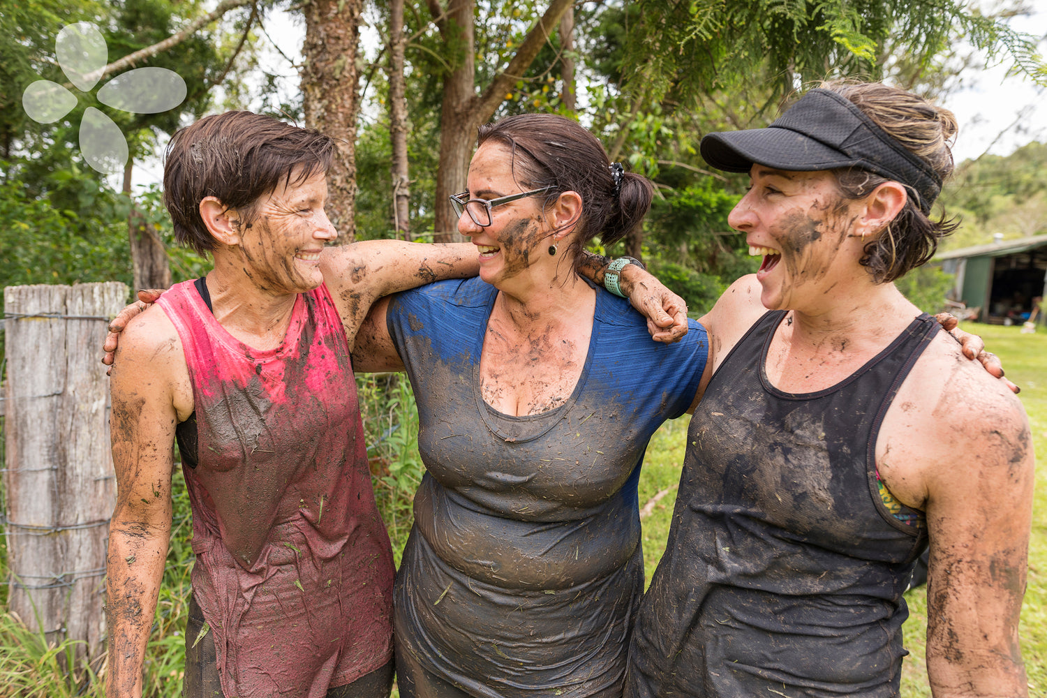 Group of 3 women covered in mud laugh with their arms around each other