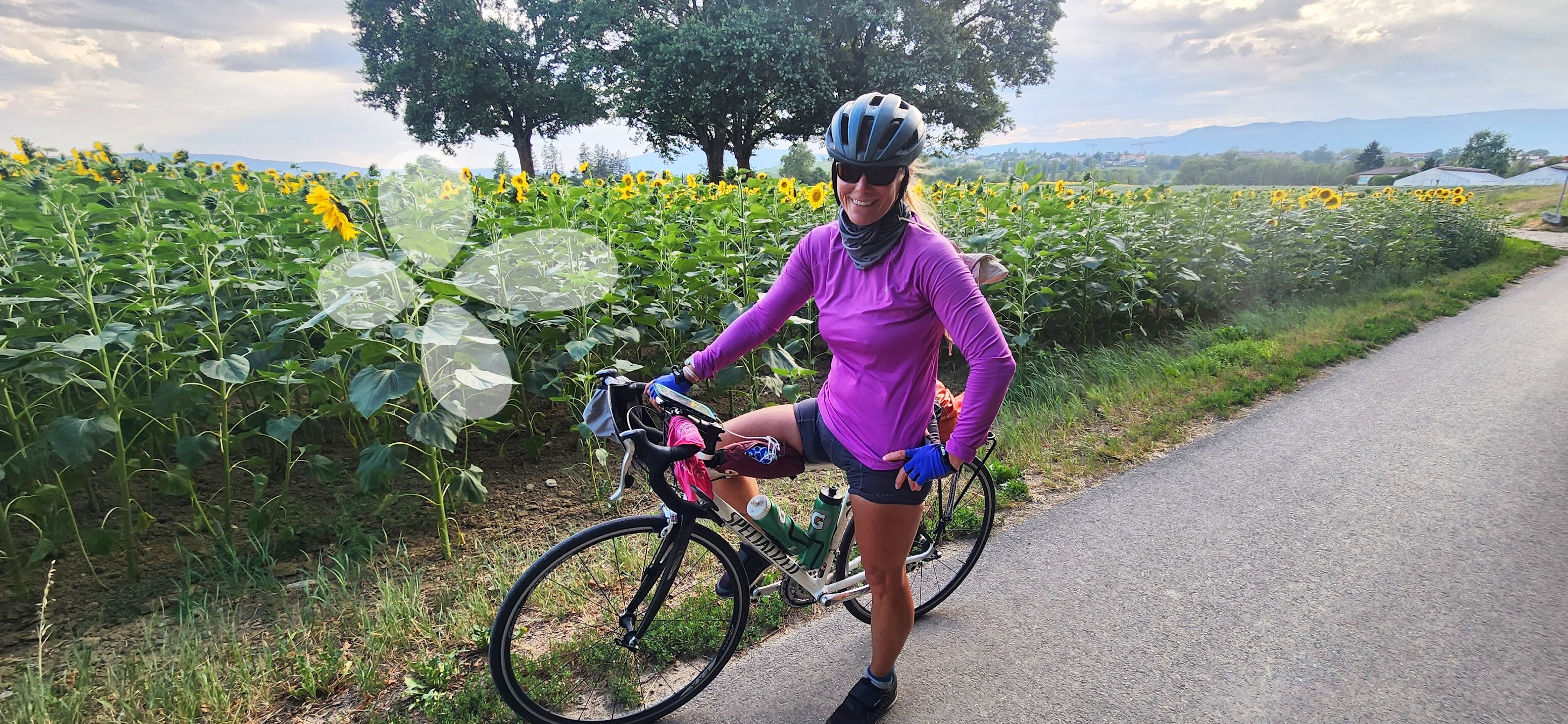 Cynthia poses with her bike on a road flanked with sunflowers